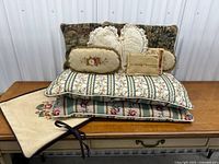 Front view of stacked vintage and antique decorative pillows showing floral needlepoint, embroidered designs, and crocheted lace pillows.
