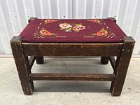 Side angle view of the footstool showing oak frame and burgundy floral needlepoint upholstery.