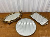 Set of three vintage and antique mirrored vanity trays on wooden surface.