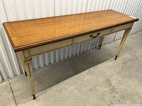 Front angle view showing full length of wooden desk with painted gilt legs and brass feet, highlighting the natural wood top and drawer pulls.