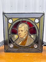 Full view of square stained glass window showing central portrait of Sir Walter Scott, surrounded by colored glass panes and bullseye glass corners