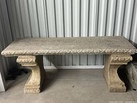 Full front view of vintage stone bench showing rectangular top with carved floral and ribbon details and two curved legs.