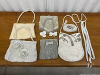 All six vintage white and silver beaded evening bags arranged on wooden surface showing variety of styles and sizes.