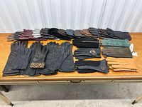 Top-down view of 18 pairs of women's leather and suede gloves in various colors and styles on a wood table