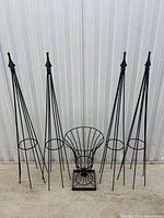 Full view of four tall wrought iron plant stands with circular ring near midpoint and one smaller wire trellis with fan shape, all with pointed finials on top.