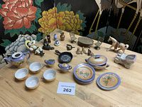 Overview of entire lot showing porcelain tea set pieces, cast iron pans, brass furniture, figurines, pull toy horse and small bottles