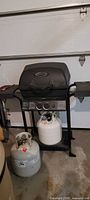 Full view of the Huntington gas grill with one propane tank attached and a second propane tank on the floor beside it.