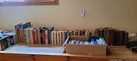Wide shot of the entire book lot arranged on a wooden surface showing dozens of books in various sizes and conditions.