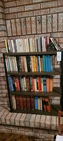 Full view of the metal bookshelf containing assorted books placed against a brick wall.