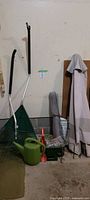 Lot showing two garden rakes, watering can, patio umbrella, and additional garden accessories.