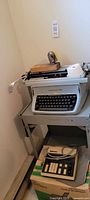Side angle view of vintage Underwood typewriter on metal desk cart showing tape dispenser and paper towel roll