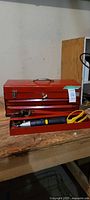 Red metal toolbox closed with top drawer open showing a yellow handled plier, an adjustable wrench, and a black/gray torque wrench inside.