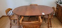 Full view of maple oval dining table with one insert and 5 chairs arranged around it