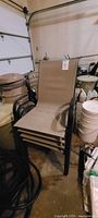 Four taupe patio chairs stacked in a garage, showing black metal frames and fabric seats.