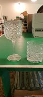 Single tall goblet with crystal look plastic and decorative cut pattern on a green table.