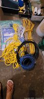 Multiple coils of electrical cords in yellow, black, and blue, small white rope, and packaged tarps on floor.
