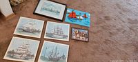 Wide view showing six plaques arranged on carpet: five sailboat plaques, one kids sailboat rug hook art plaque, one puppy photo plaque