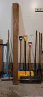Photo showing various shovels with colored plastic D-grip handles, a large wooden plank, and metal roller tool.