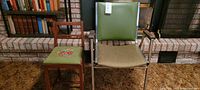 Two chairs side by side in front of fireplace; child's needlepoint upholstered wooden chair and vintage green office chair