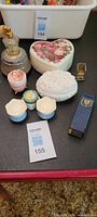 Overview photo showing all dresser items grouped together: perfume atomizer, heart-shaped floral box, white floral sculpted box, small containers including painted portrait container, square metal container, and a rectangular navy box.