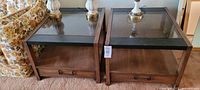 Two large vintage Mid-Century Modern style end tables with smoked glass tops and wooden frames with lower storage drawers.