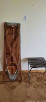 Vintage wooden ironing board folded and standing on its narrow side, grey fabric cover visible, wood grain visible on underside supports.