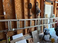 Aluminum extension ladder hanging horizontally on wall in a wooden shed with other tools and items around.
