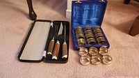 Carving set in black case and napkin rings in lined blue box with extra loose rings on carpet