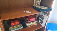 Books and art prints on wooden shelves showing titles and artwork with minor edge wear
