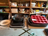 Overview photo of assorted metal cake pans, baking trays, and silicone muffin tin on table in basement.