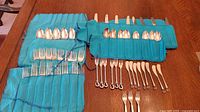 Two blue cloth storage rolls and all flatware pieces laid out on table