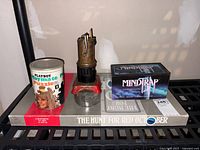 Photo showing Playboy Playmate Puzzle container, vintage mechanical object, Mindtrap game, and The Hunt for Red October game stacked beside each other on a shelf.