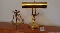 Brass piano light and lyre-shaped brass book stand shown together with a price tag on wooden surface.