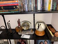 Photo showing the Bulova clock with marble base, wedding couple snow globe on wooden base, and bagpiper figurine placed together on a shelf with other items.