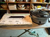 Cuisinart warming tray on the left with original box alongside Crock-Pot slow cooker on the right on a folding table in a basement setting.