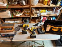 Full set of DeWalt cordless drill tools laid out on a table. Visible are two cordless drills, two battery packs, a battery charger, a wire brush, and a carrying bag.