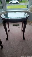 Front angle view of round glass-top end table showing wood frame and curved legs.