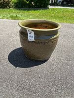 Green ceramic plant pot photographed outdoors on pavement, showing body and flared rim with patterned design.