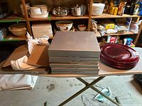 View of all 10 red plates stacked next to their original boxes on a folding table in a basement storage area.