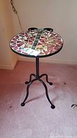 Full view of round ladybug mosaic tile accent table on metal frame base with three curved legs.