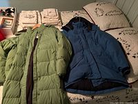 Two women's winter coats laid out on bed: one green L.L. Bean puffer jacket and one blue MEC parka