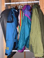 Six outerwear jackets and windbreakers hanging on a rack in various colors and styles.
