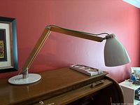Full view of the mid-century modern desk lamp on a wooden desk with red wall background.