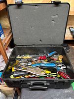 Top view of the open black hard plastic case filled with mixed hand tools showing handles in multiple colors and large locking pliers on top.