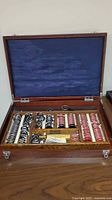 Full view of the open wooden case with blue lining showing assembled optometry lenses and accessories inside.