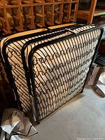 Folded metal frames of two folding beds showing spring mattress support layers.