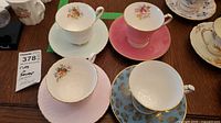 Set of 4 bone china teacups and saucers laid out on a wooden surface showing various floral and gold trim designs, with pink, white, and blue saucers.