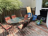 Full view of patio set on wooden deck including table, six chairs with cushions, and storage box