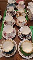 View showing eight Royal Albert bone china teacup and saucer sets arranged on a table, displaying varied floral patterns and gold accents.