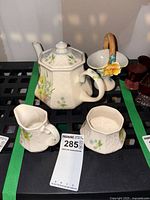 The full tea set on display including teapot, creamer, sugar bowl, and decorative basket, showing embossed floral patterns and painted flower details.